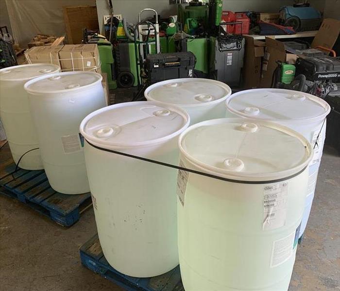 Six white barrels in a garage with SERVPRO equipment. 