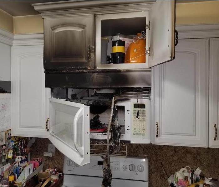 White microwave and white cabinets burned and covered in soot